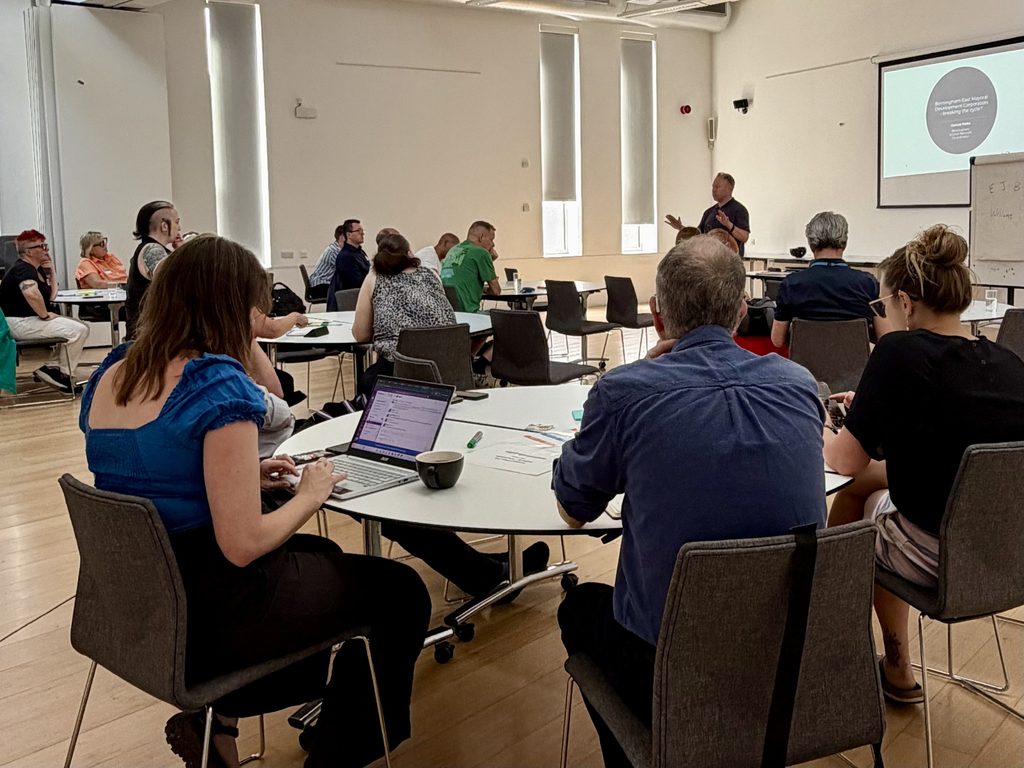 A group of people seated at tables in a conference room, attending a presentation.